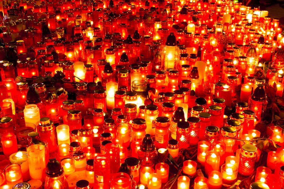 Numerous red and white candles of various sizes are lit, creating a warm, glowing sea of light in a nighttime scene.