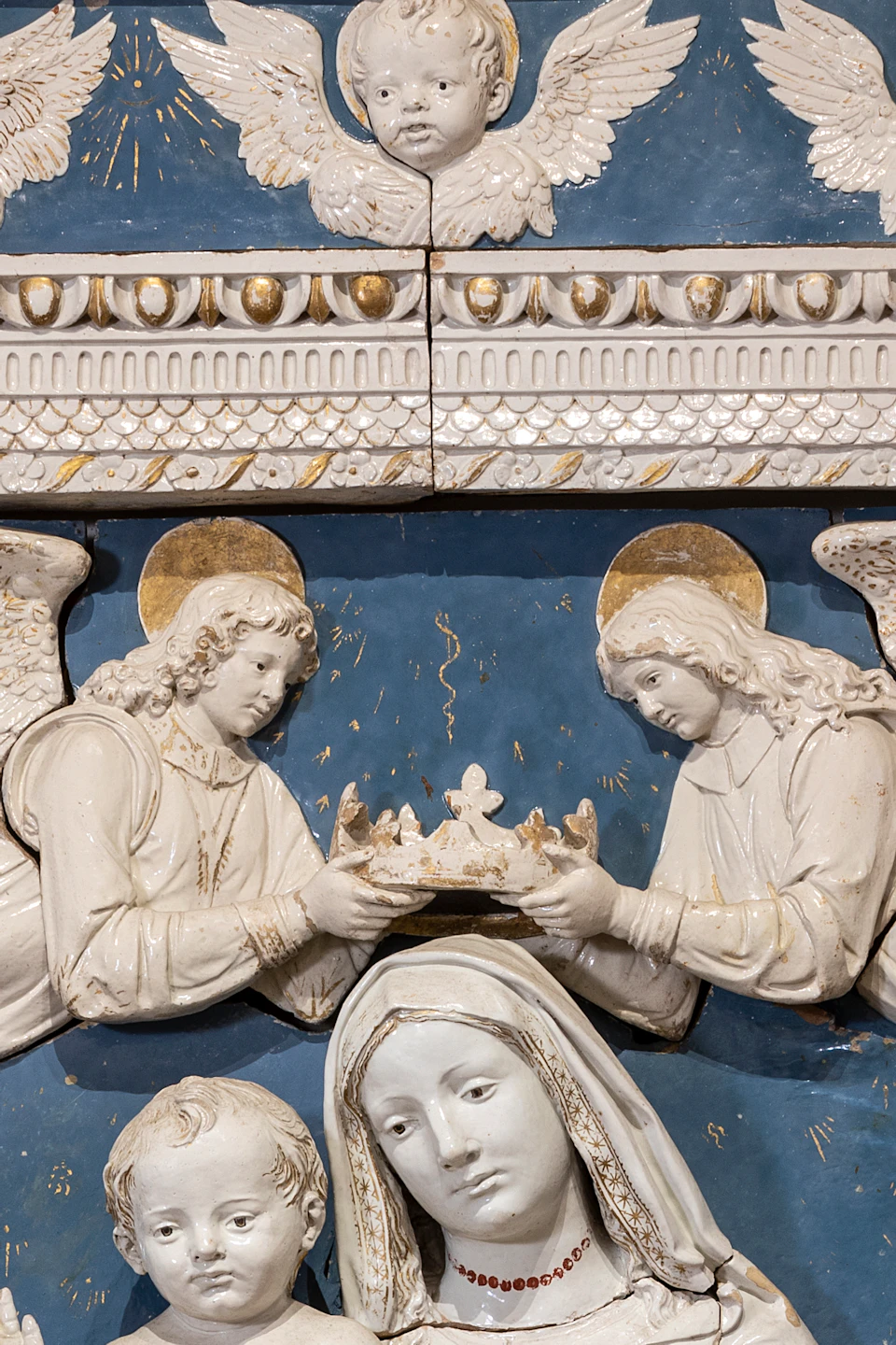 A detailed relief depicting religious figures, including a seated Madonna with child, flanked by two saints, with angels overhead.
