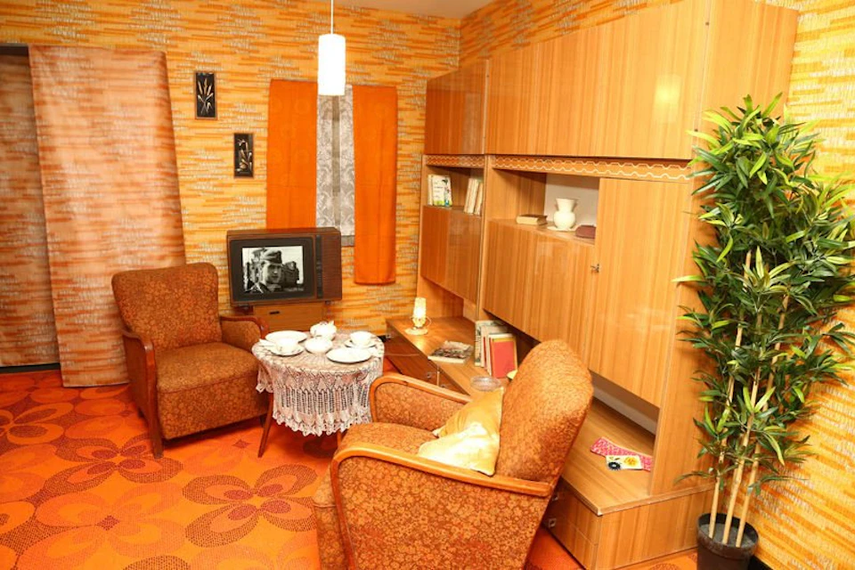 A retro living room with orange furniture and decor, a TV displaying a black-and-white image, a small table with tea set, and wooden cabinets.