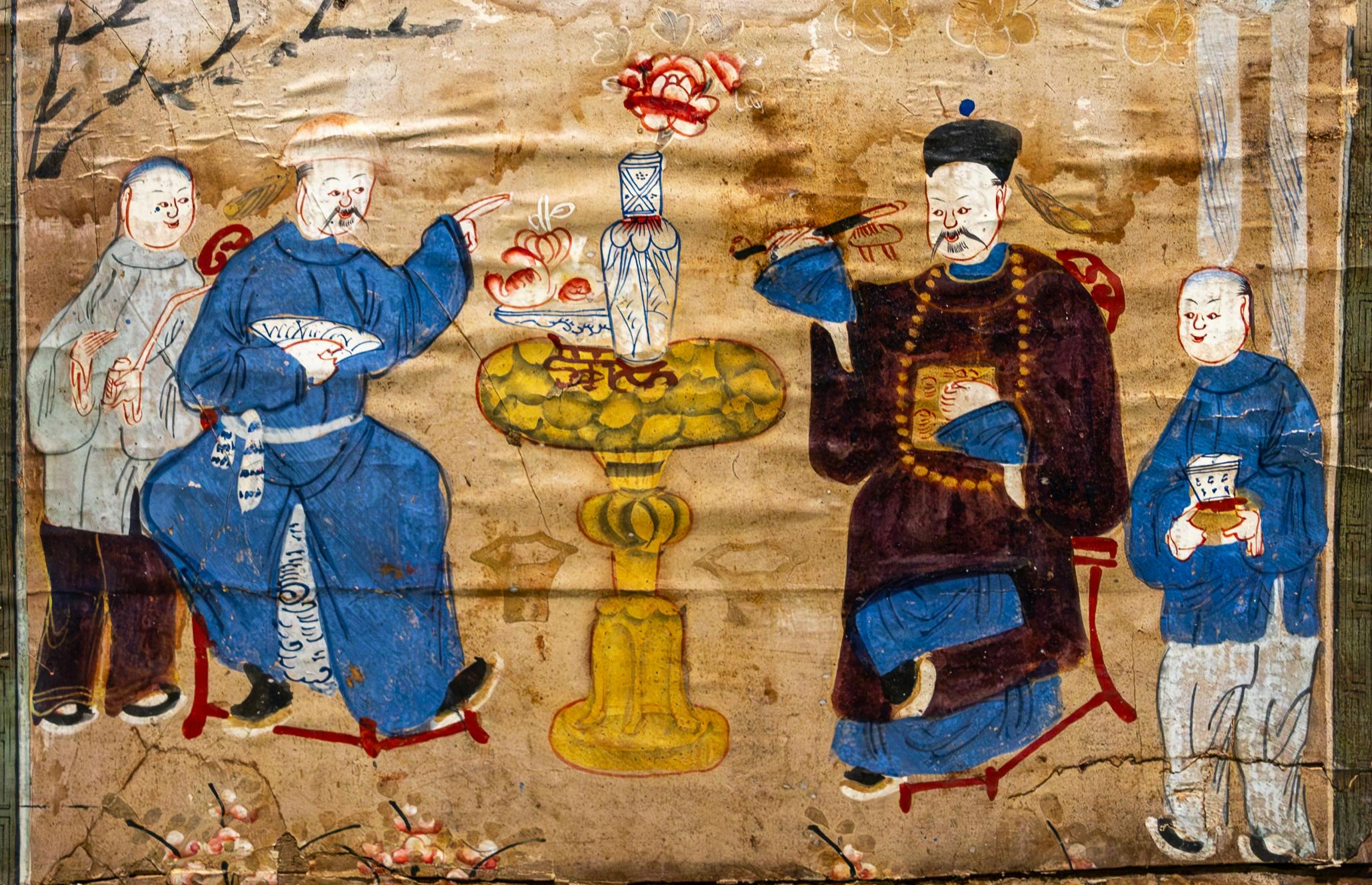 En målning i traditionell stil som visar fyra figurer sittande runt ett bord med mat och en vas, placerad på en strukturerad bakgrund.