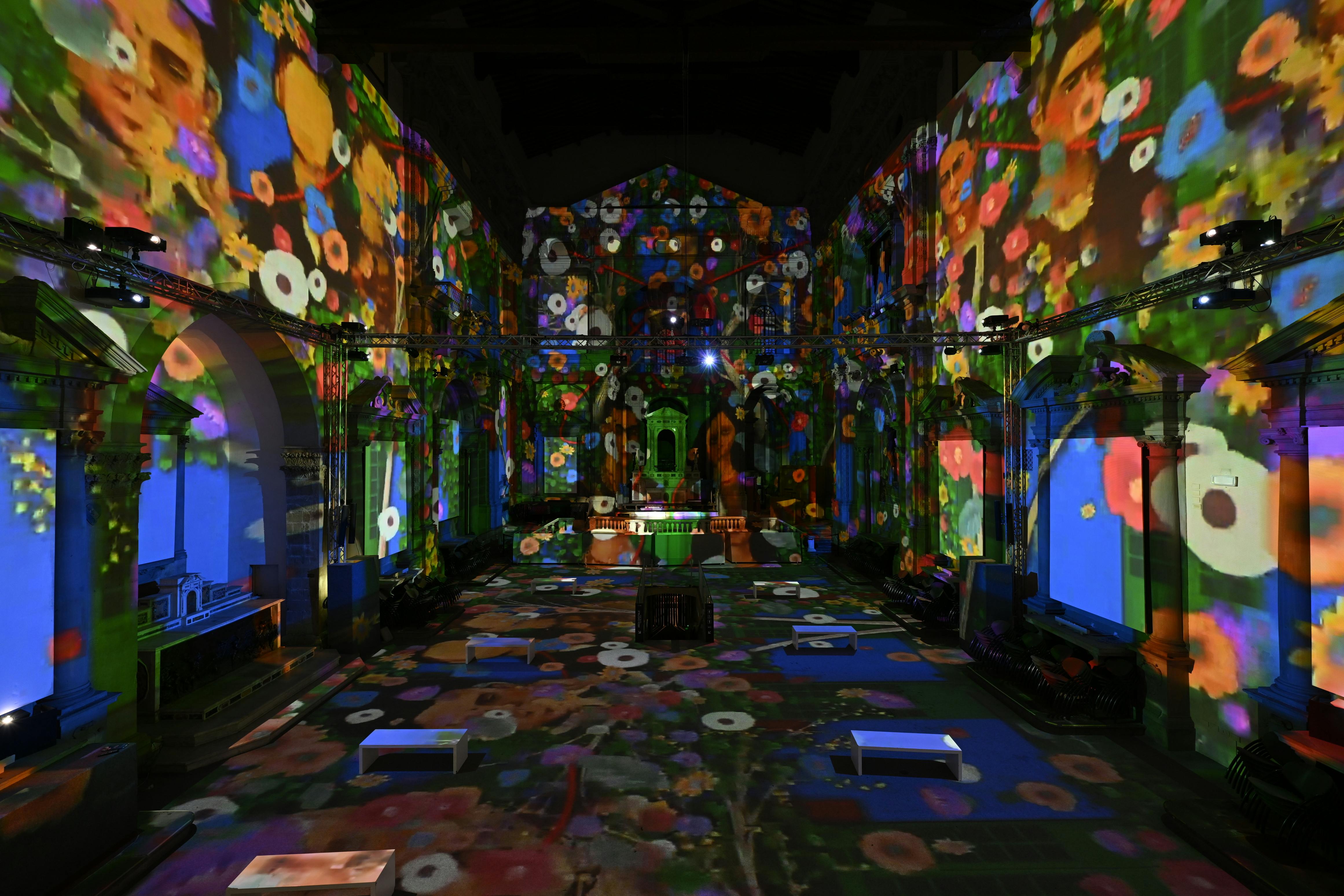 A vibrant art installation inside a hall, projecting colorful flower patterns onto the walls and floor.