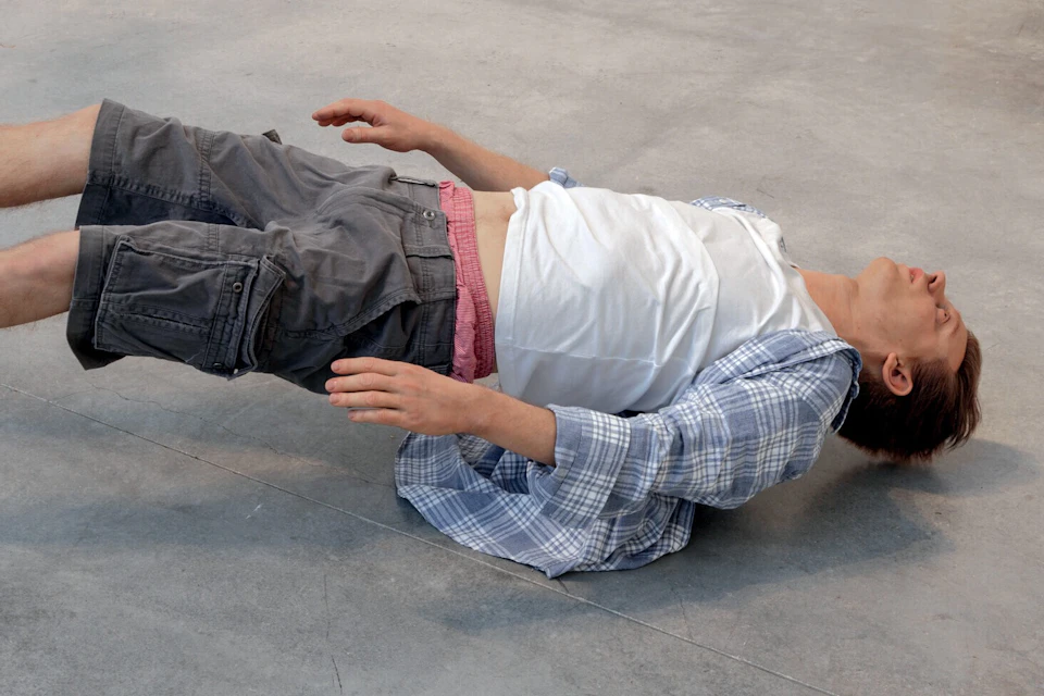 A person in casual clothing lies on their back on a flat concrete surface.