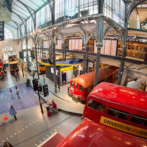Innenraum eines Verkehrsmuseums mit alten roten Bussen, einem U-Bahn-Wagen, Informationsdisplays und Besuchern, die die Exponate erkunden.