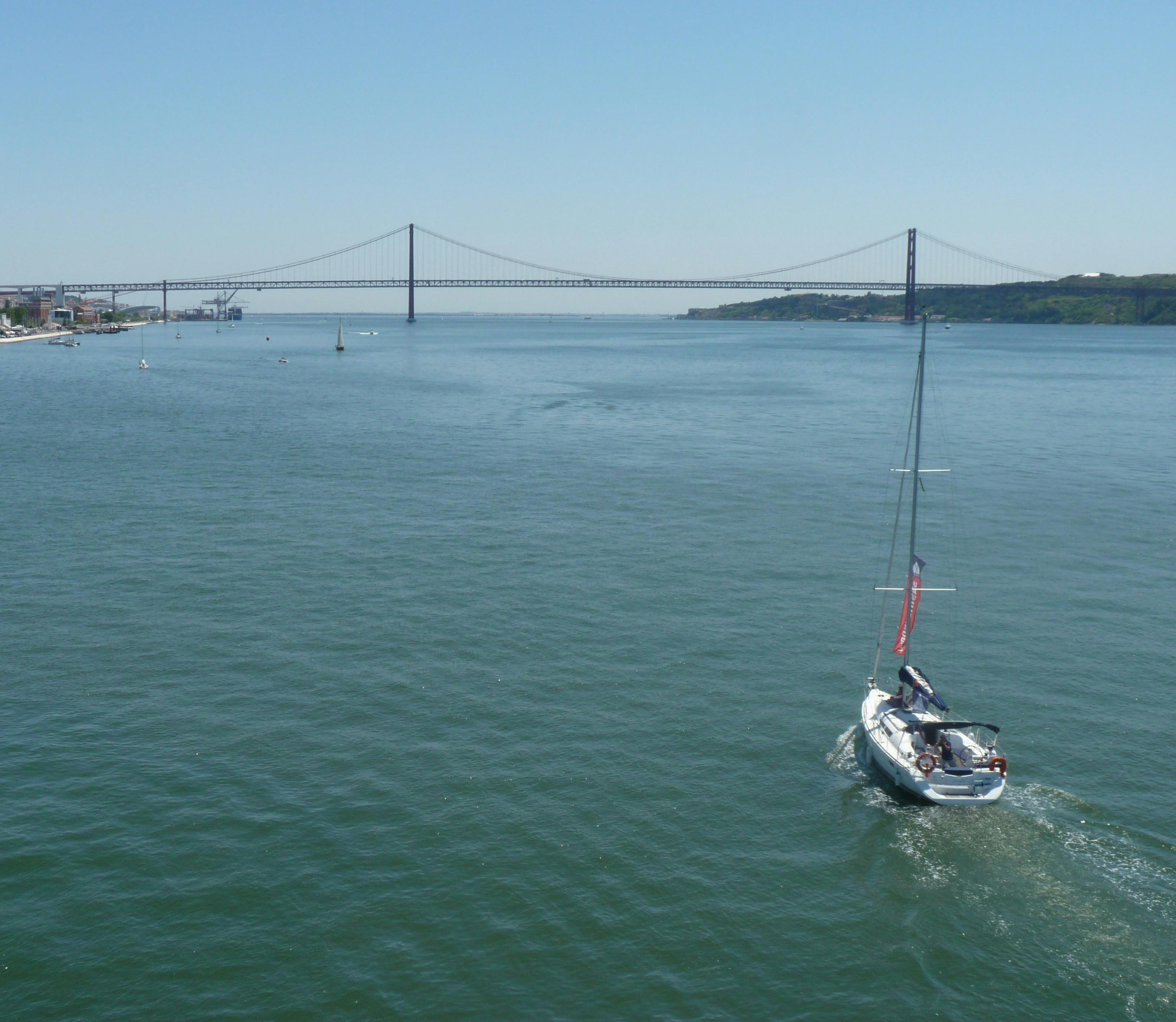 맑고 푸른 하늘 아래 먼 현수교를 향해 잔잔한 물 위를 이동하는 범선.