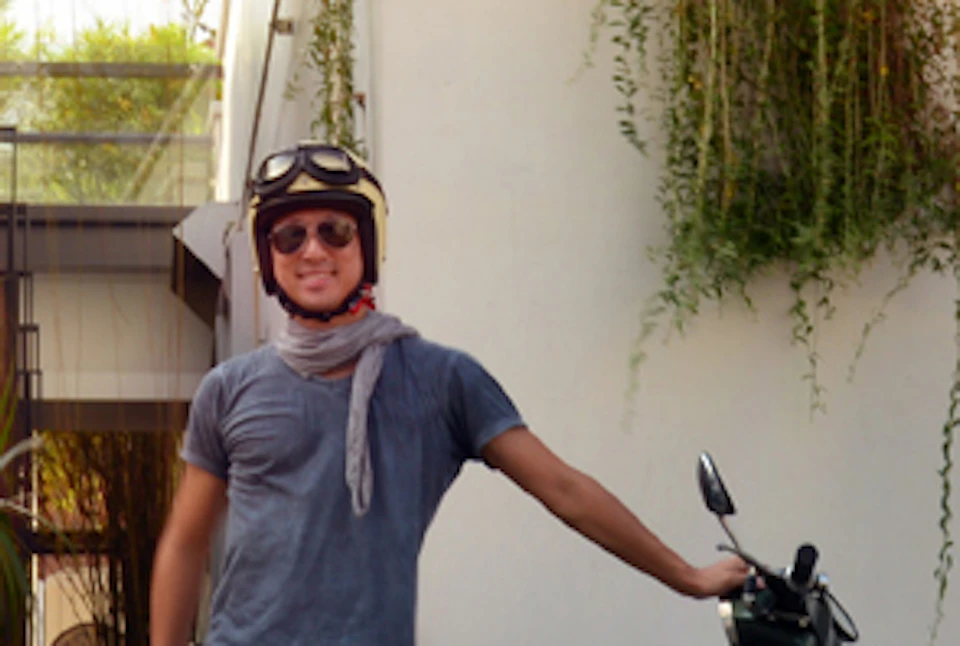 Three people standing with motor scooters in front of a building with greenery on the wall; one person in a sidecar.