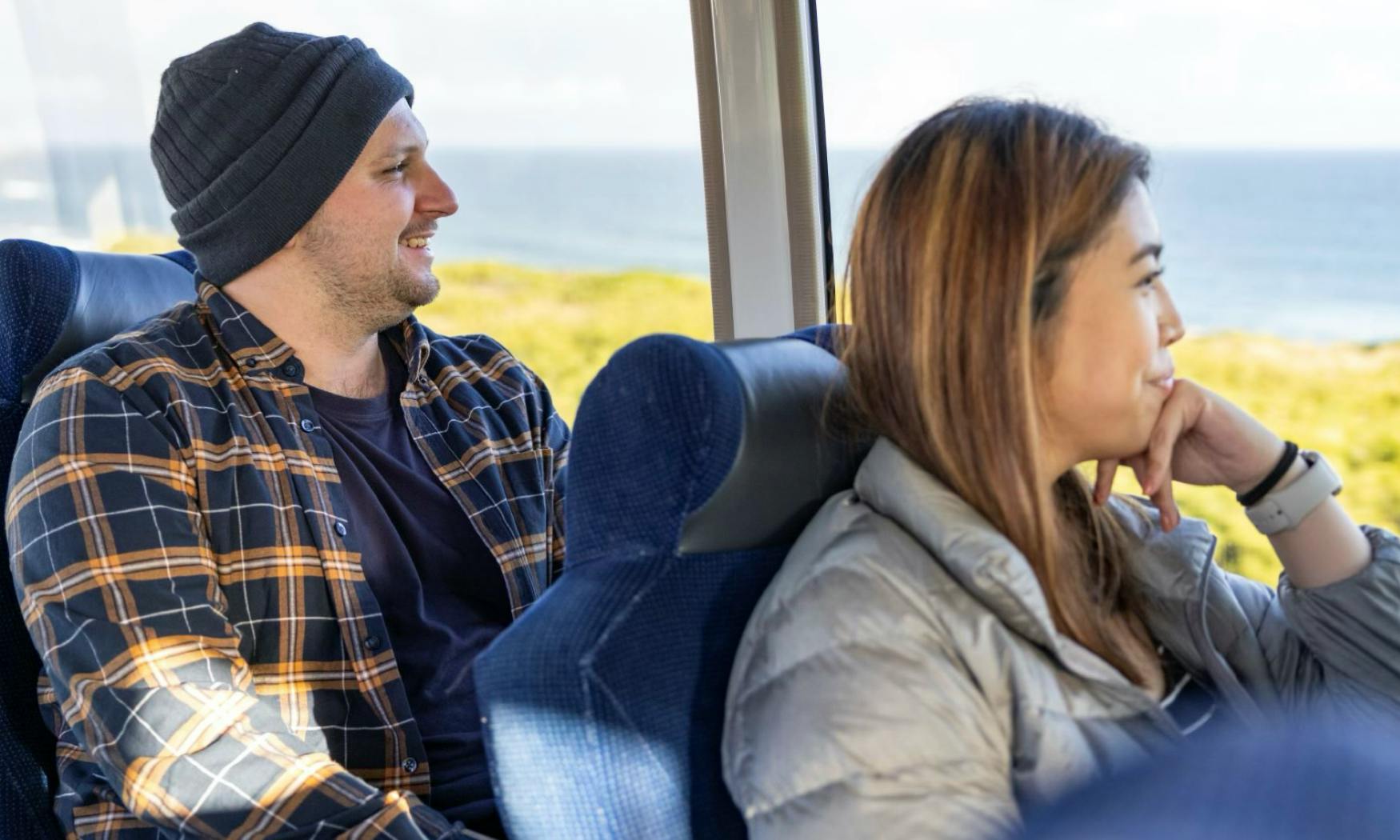 Δύο άτομα κάθονται σε ένα κινούμενο όχημα με μια γραφική θέα στον ωκεανό ορατή μέσα από τα παράθυρα.