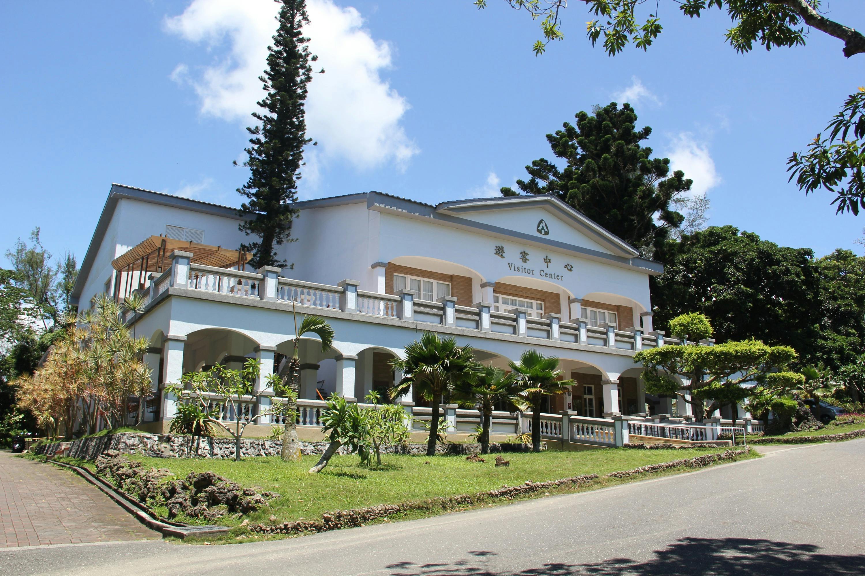 A two-story visitor center building surrounded by trees, with a sunny sky and a road in the foreground.