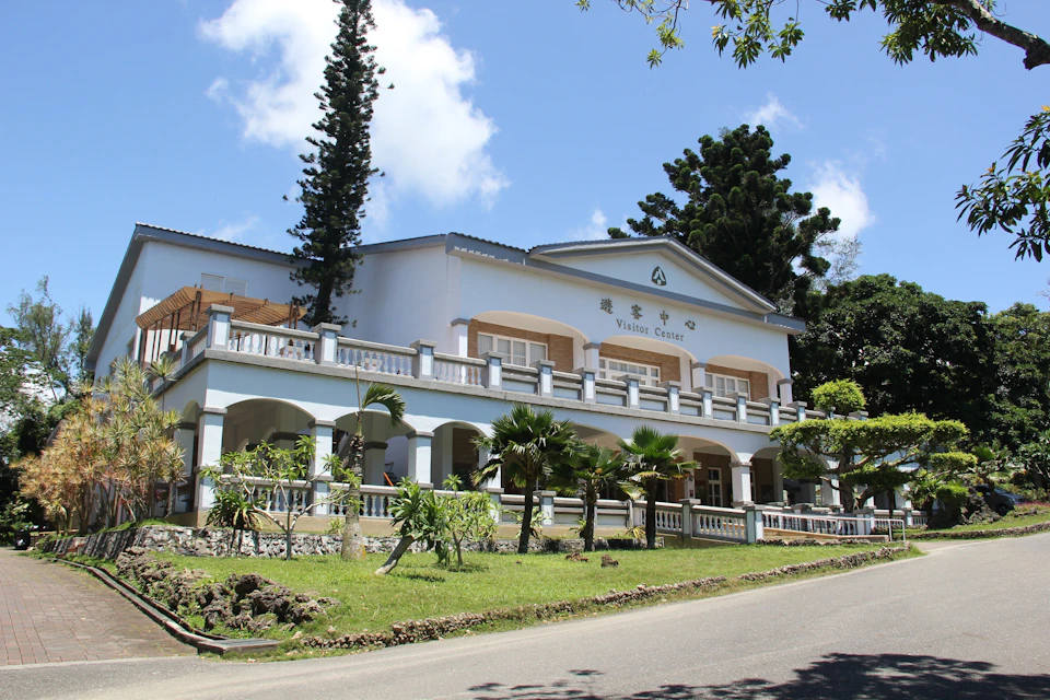 A two-story visitor center building with arched windows and a balcony, surrounded by lush greenery and tall trees.