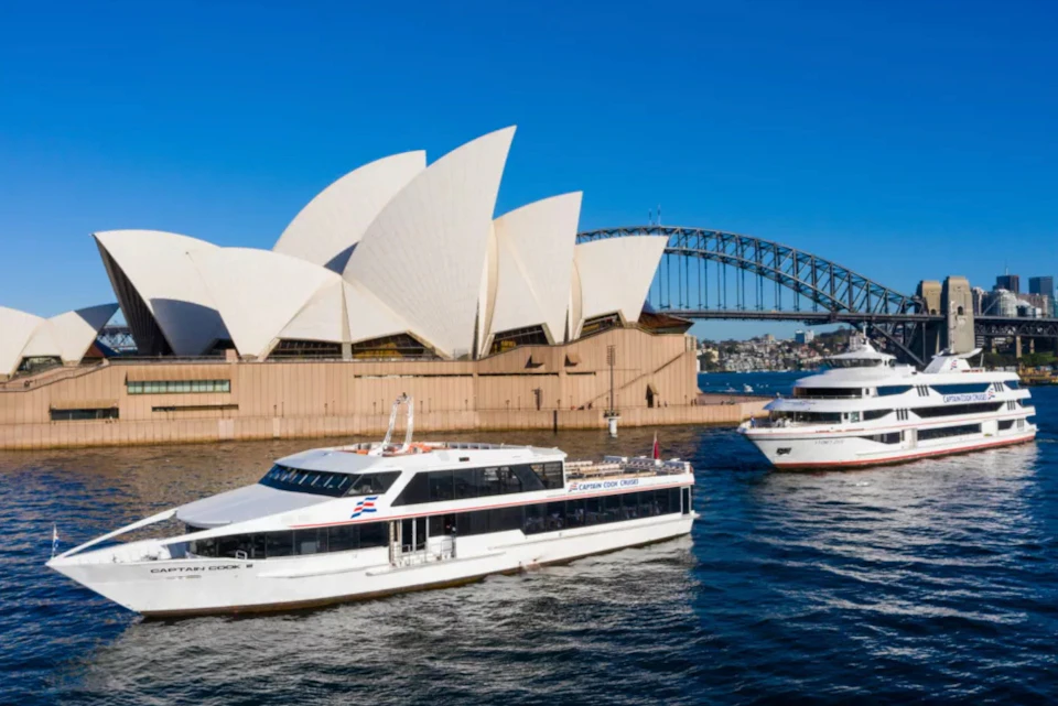 Two boats sail near the Sydney Opera House and Sydney Harbour Bridge on a sunny day.