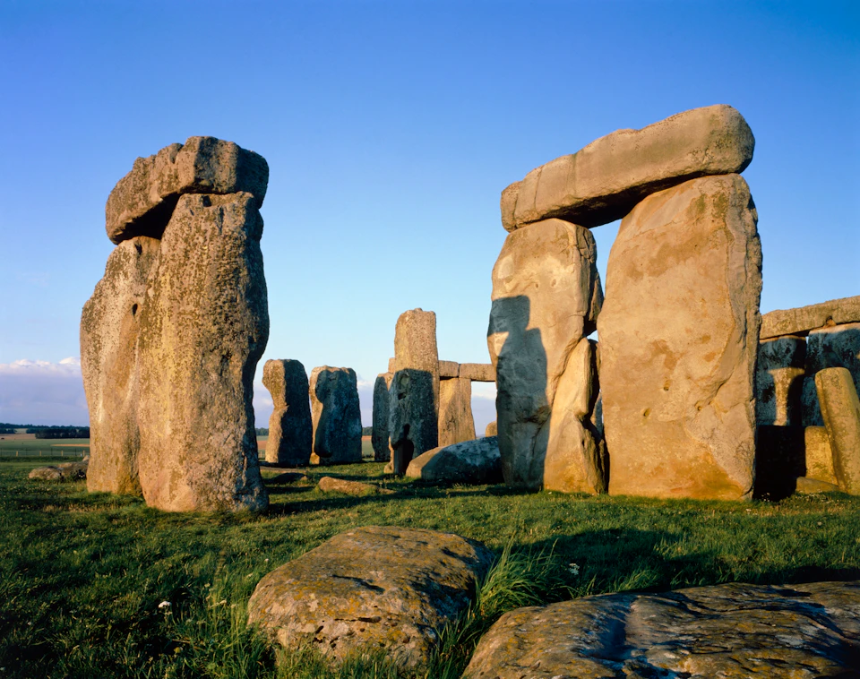 Stonehenge with large standing stones arranged in a circular pattern on a grassy field under a clear blue sky.