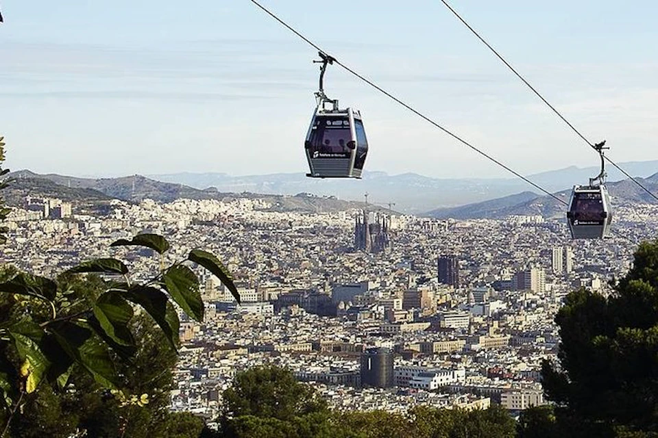 A cable car suspended in the air with a view of a cityscape and mountains in the background under a clear sky.