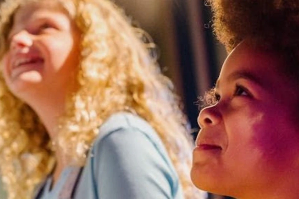 Two children smiling and engaging in an interactive activity, illuminated by bright lighting indoors.