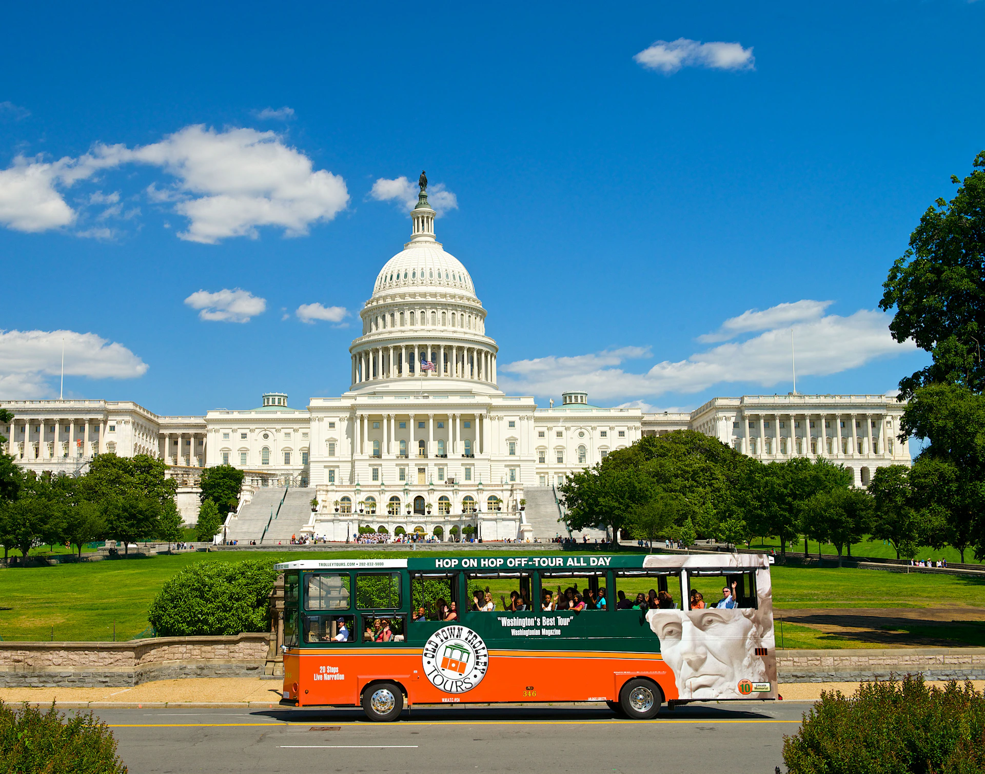 A sightseeing bus drives in front of the United States Capitol building under a clear blue sky.