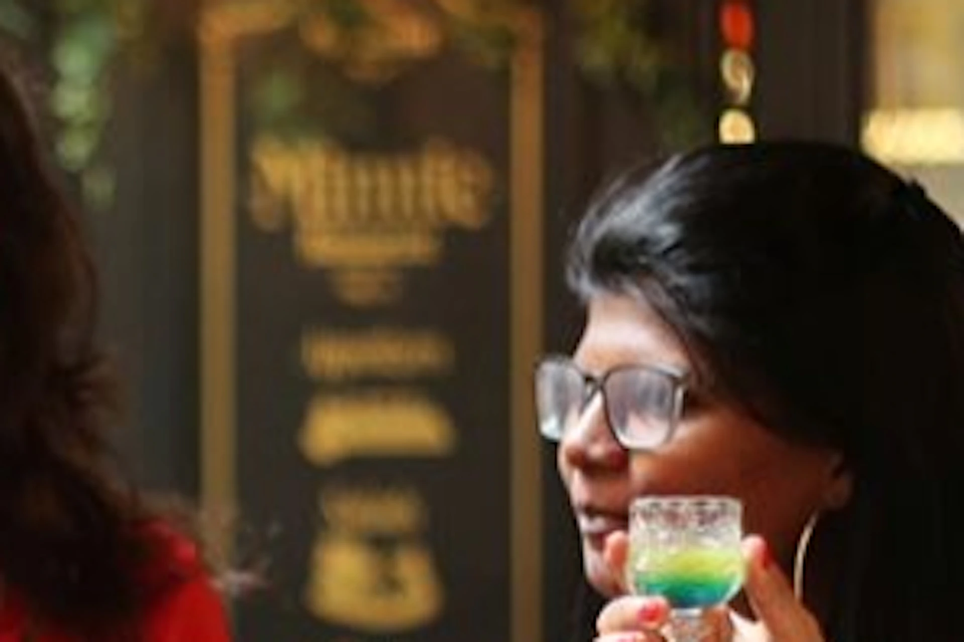 Four people stand together in a social setting, holding small glasses and engaging in conversation.