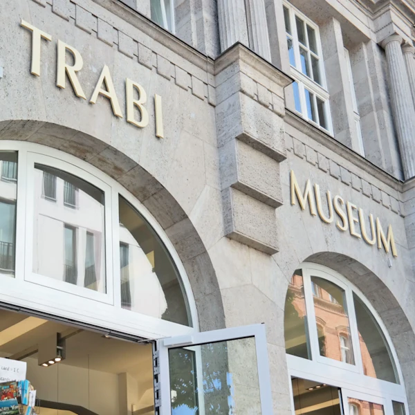 Det ydre af en bygning mærket "Trabi Museum" med store buede vinduer og en åben døråbning i bunden.