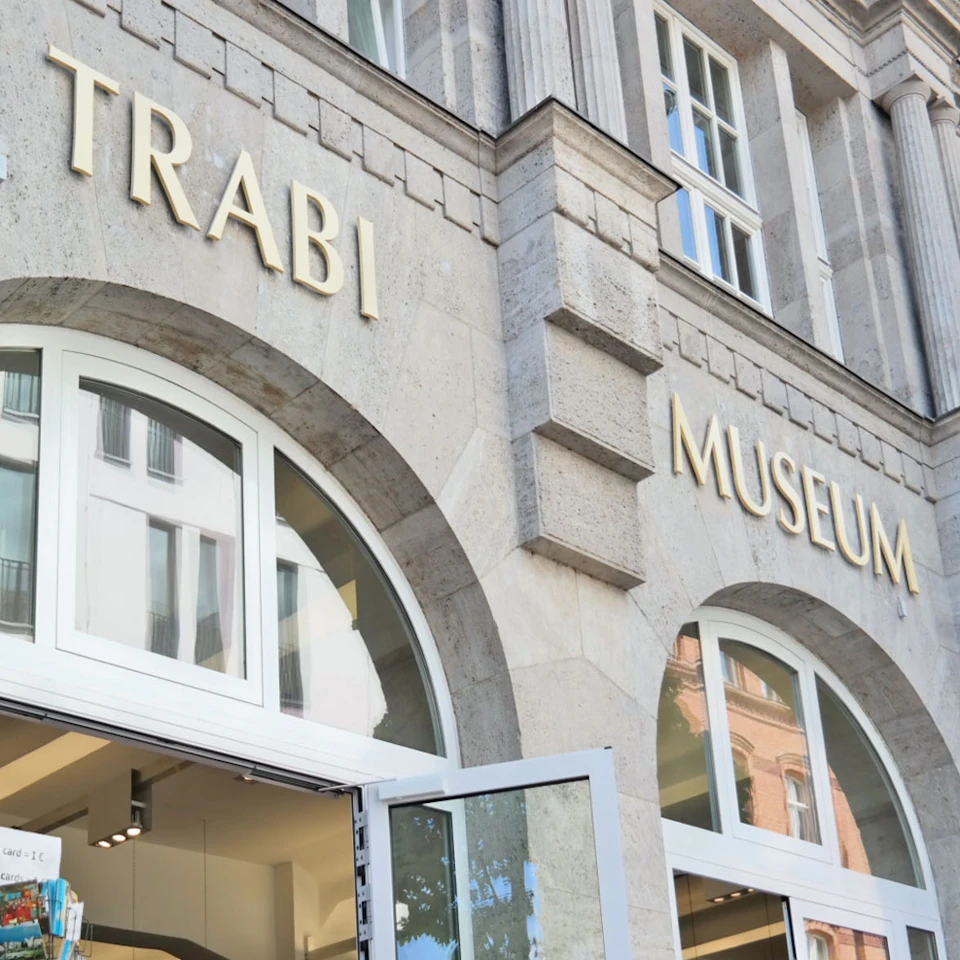 The exterior of a building labeled "Trabi Museum" with large arched windows and an open doorway at the bottom.