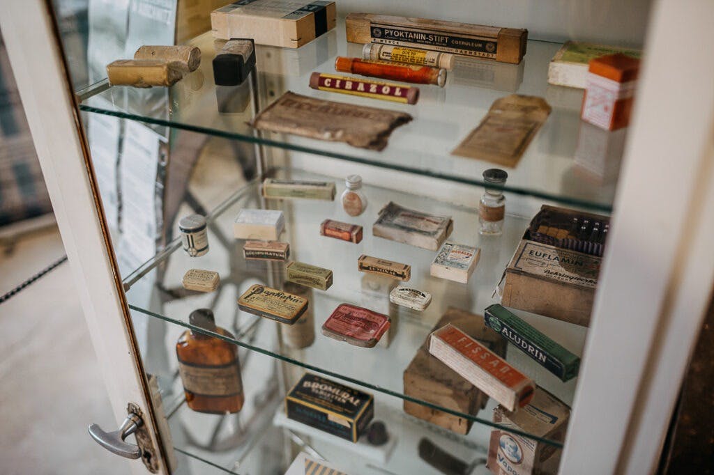 En glasdisplaykasse fyldt med forskellige medicinske og farmaceutiske vintageartikler, herunder flasker, kasser og rør.