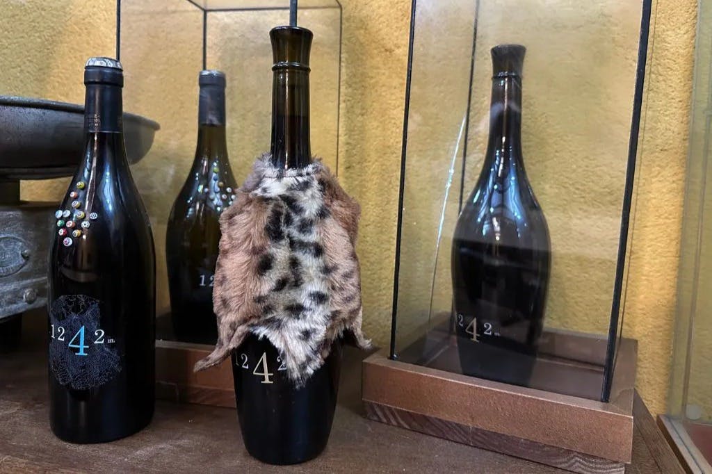 Eine mit Tierfell überzogene Weinflasche steht in einer Vitrine mit ähnlichen Flaschen im Hintergrund.
