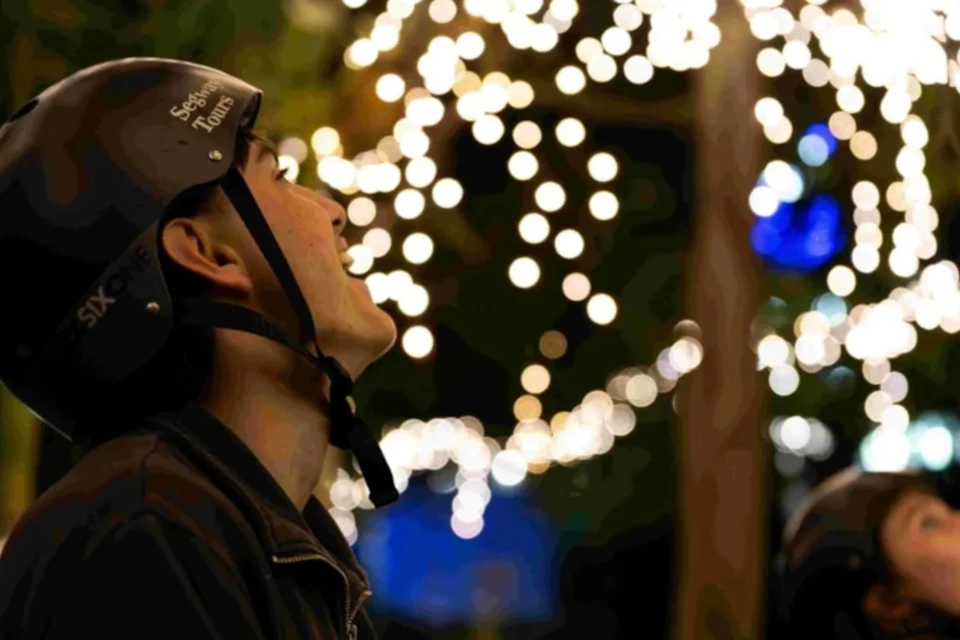 A person in a helmet looking upward, with a background of blurred, glowing lights on trees at night.