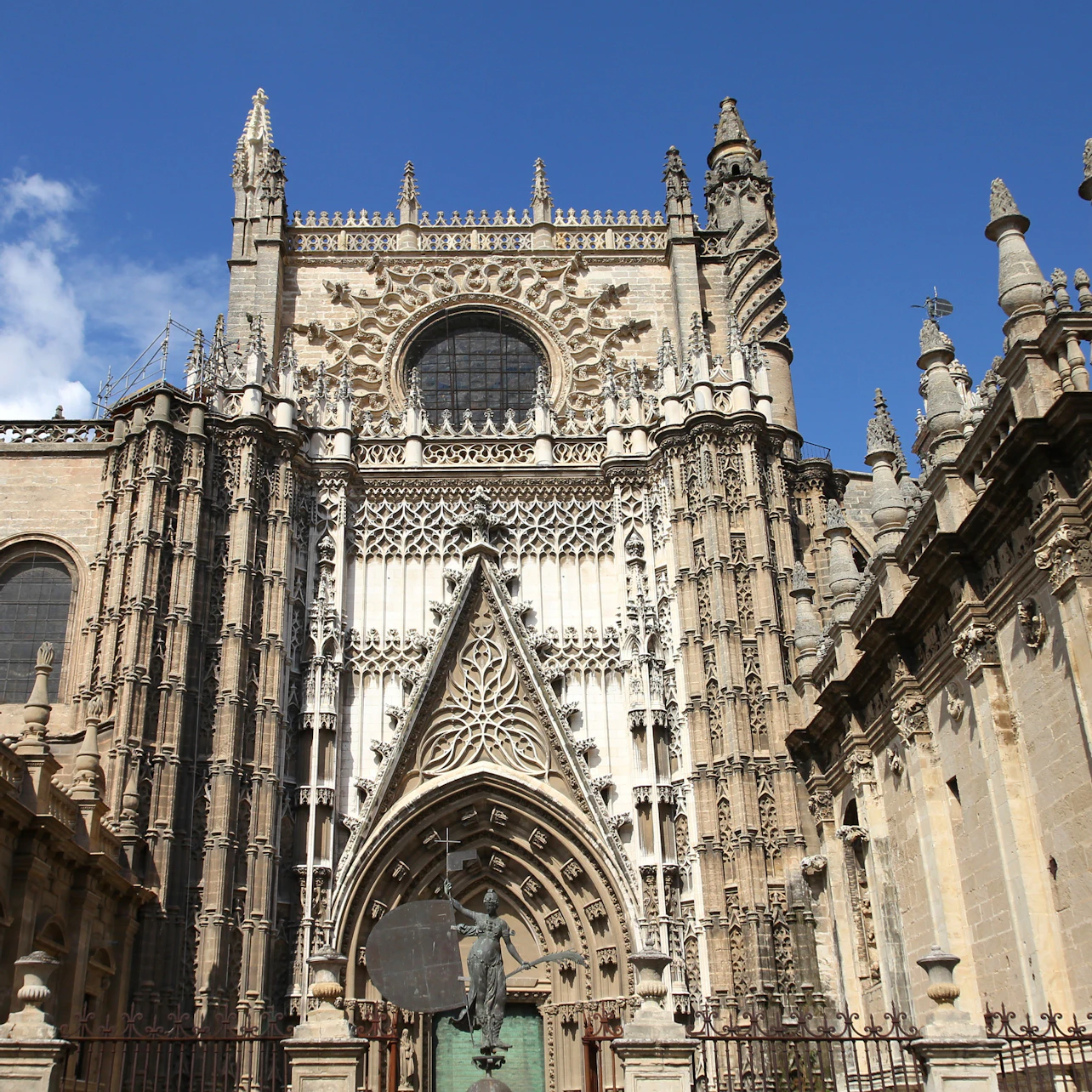 Ornate Gothic cathedral facade with detailed carvings, arches, and a central round window under a clear blue sky.