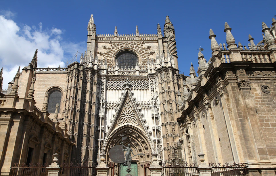 Ornate Gothic cathedral facade with detailed carvings, arches, and a central round window under a clear blue sky.