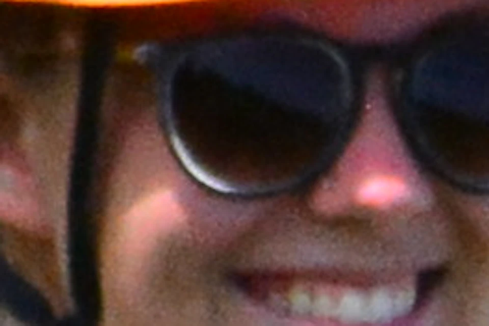 Person smiling and zip-lining through a lush green forest, wearing a helmet, harness, and pink shoes.
