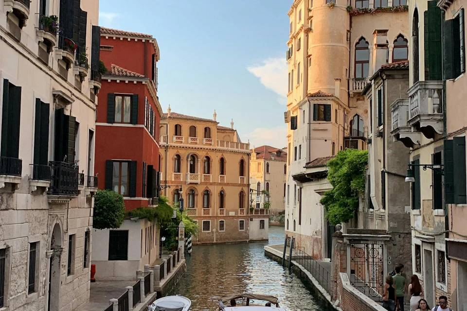 A canal in Venice lined with colorful historic buildings under a clear sky, with boats docked along the water.