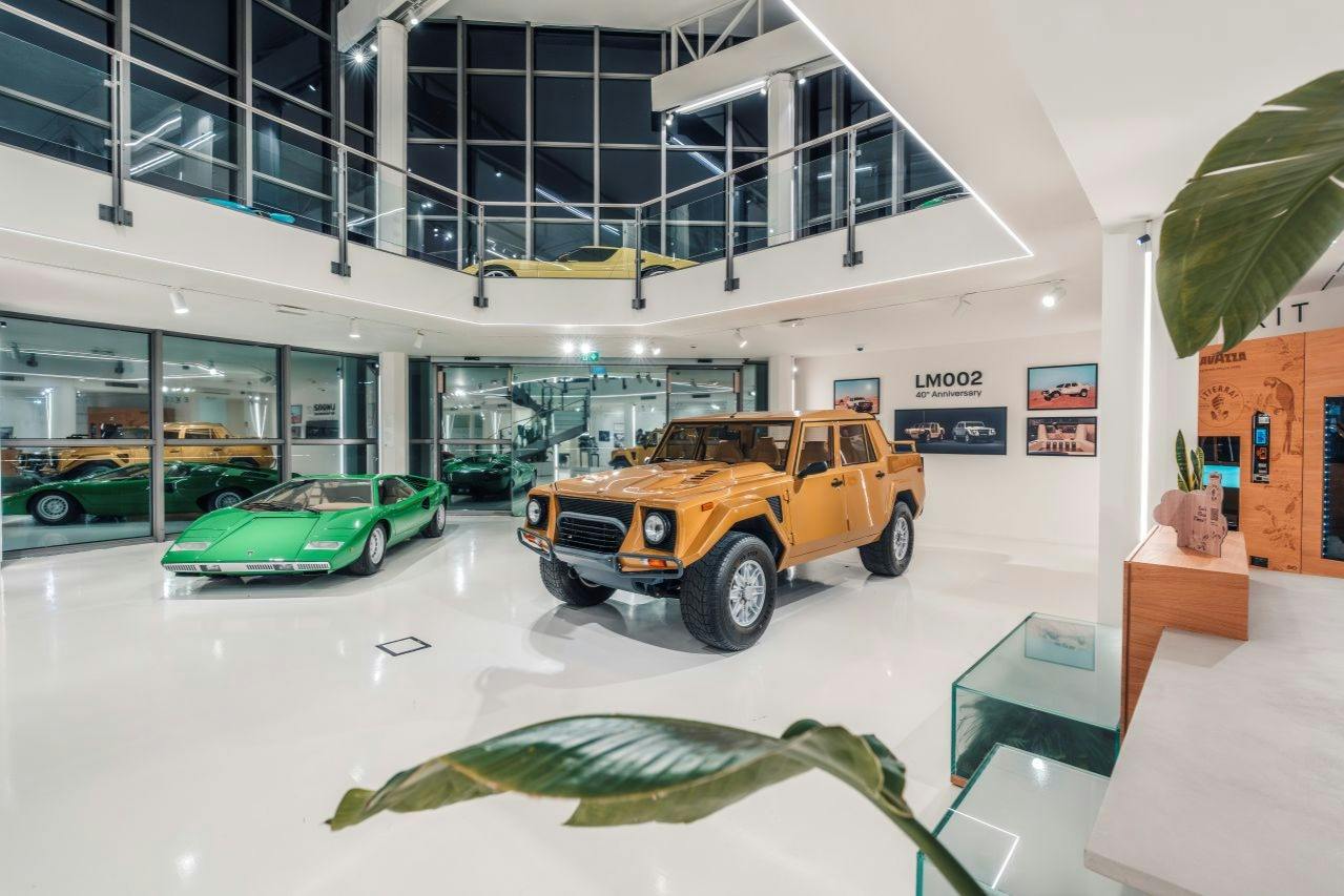 Et moderne showroom med en klassisk orange SUV og en grøn sportsvogn med slank arkitektur og glasvægge.