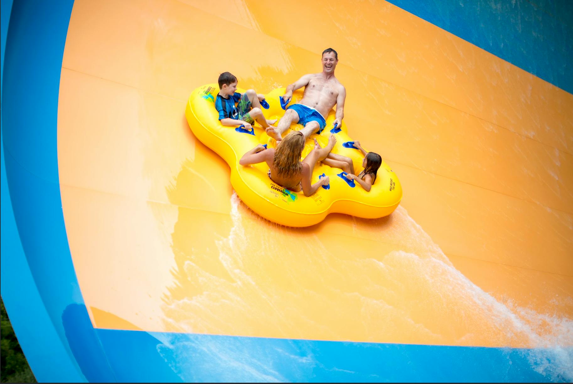 Quatre persones baixant per un tobogan d'aigua en una bassa inflable groga.