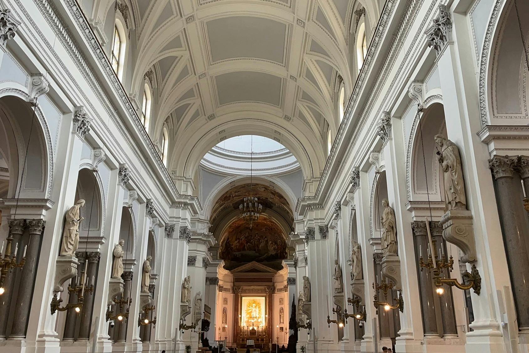 높은 아치형 천장과 화려한 기둥, 조각상, 맨 끝에 불이 켜진 제단이 있는 대성당 내부.