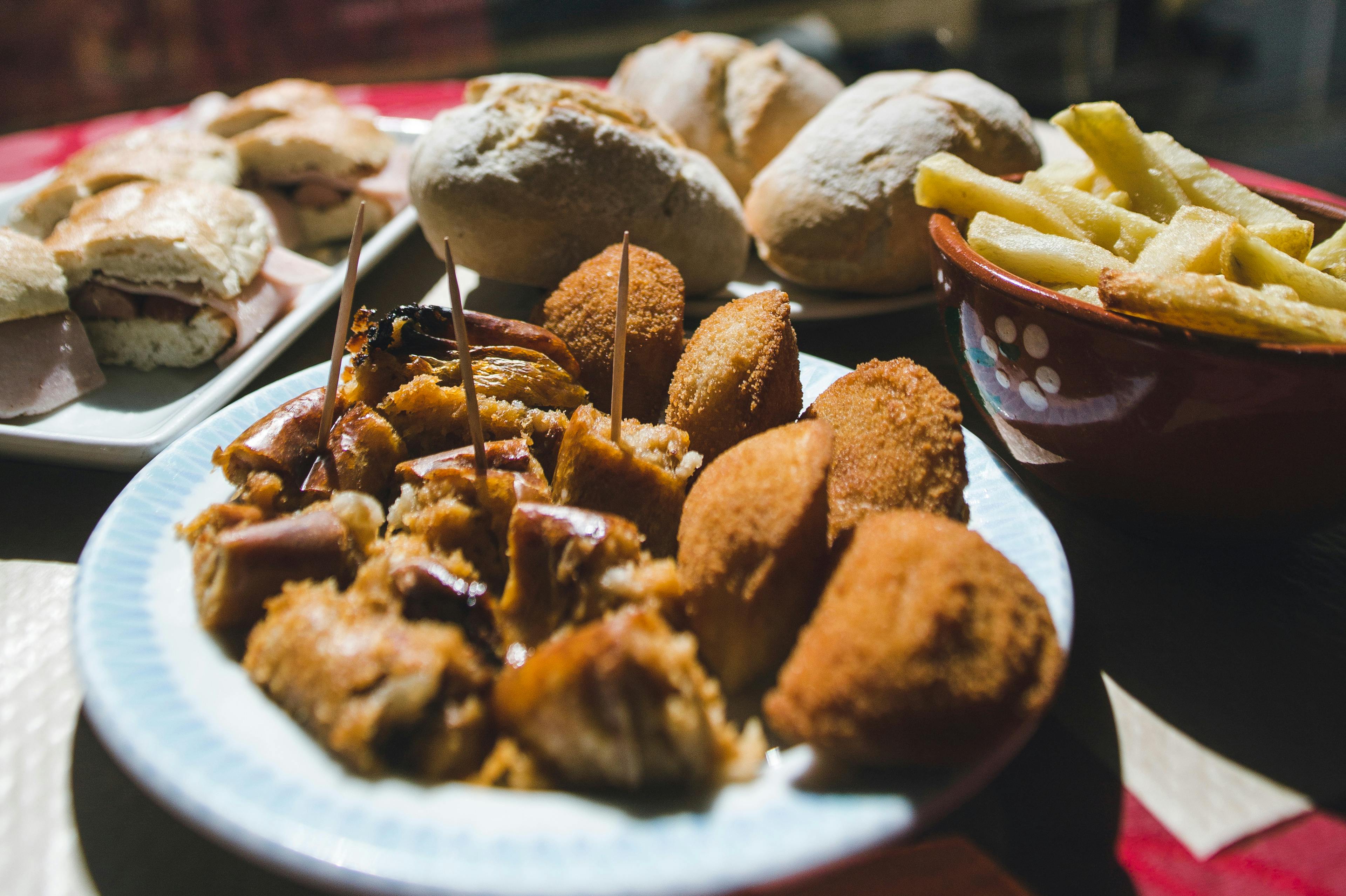 Een bord met kroketten en spiesjes, omringd door broodjes en een schaaltje friet.