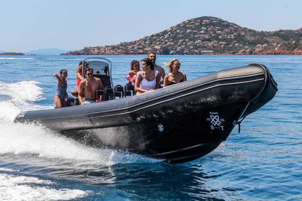 A group of people riding in a black speedboat on the ocean near a hilly coastline with houses.