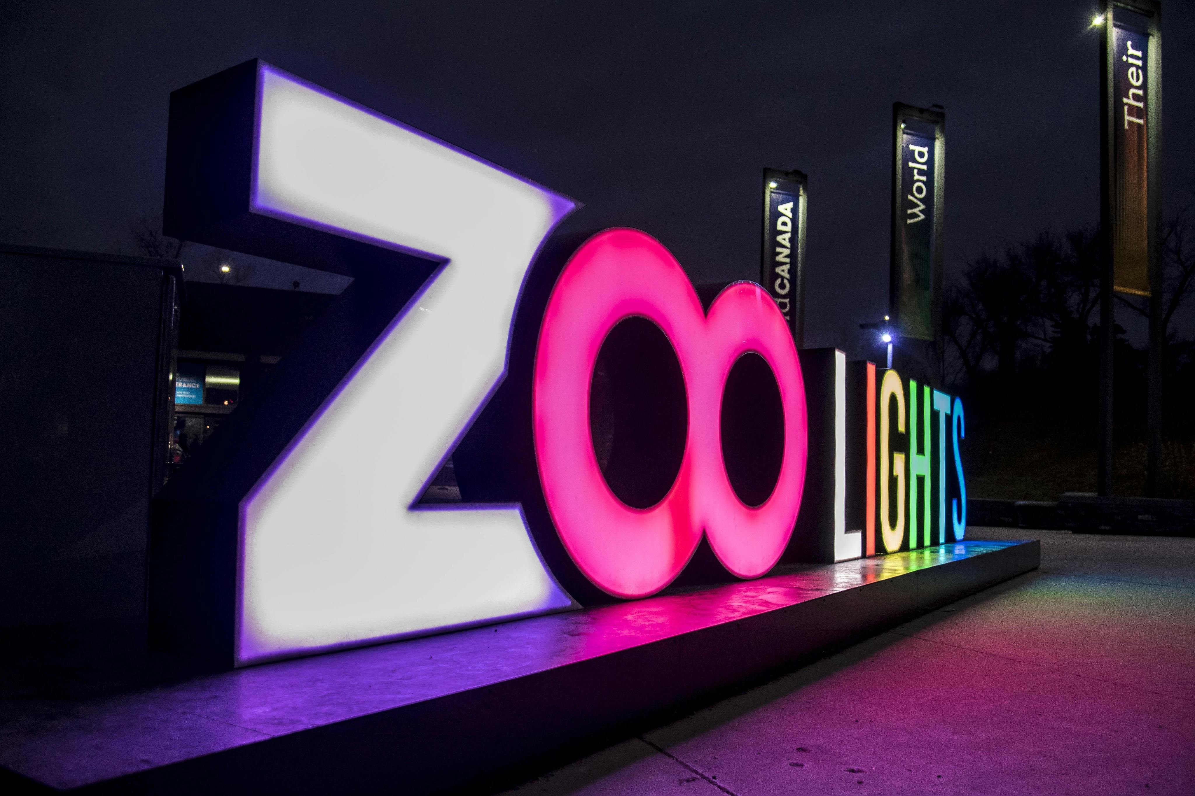 어두운 하늘을 배경으로 화려한 글씨로 "ZooLights" 를 읽는 조명 표지판. 배경에는 "Canada's Wonderland" 배너가 있습니다.