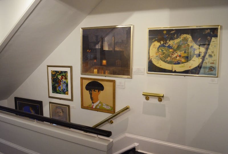 A staircase wall gallery featuring framed paintings, including a portrait of a matador, an urban night scene, and abstract art.
