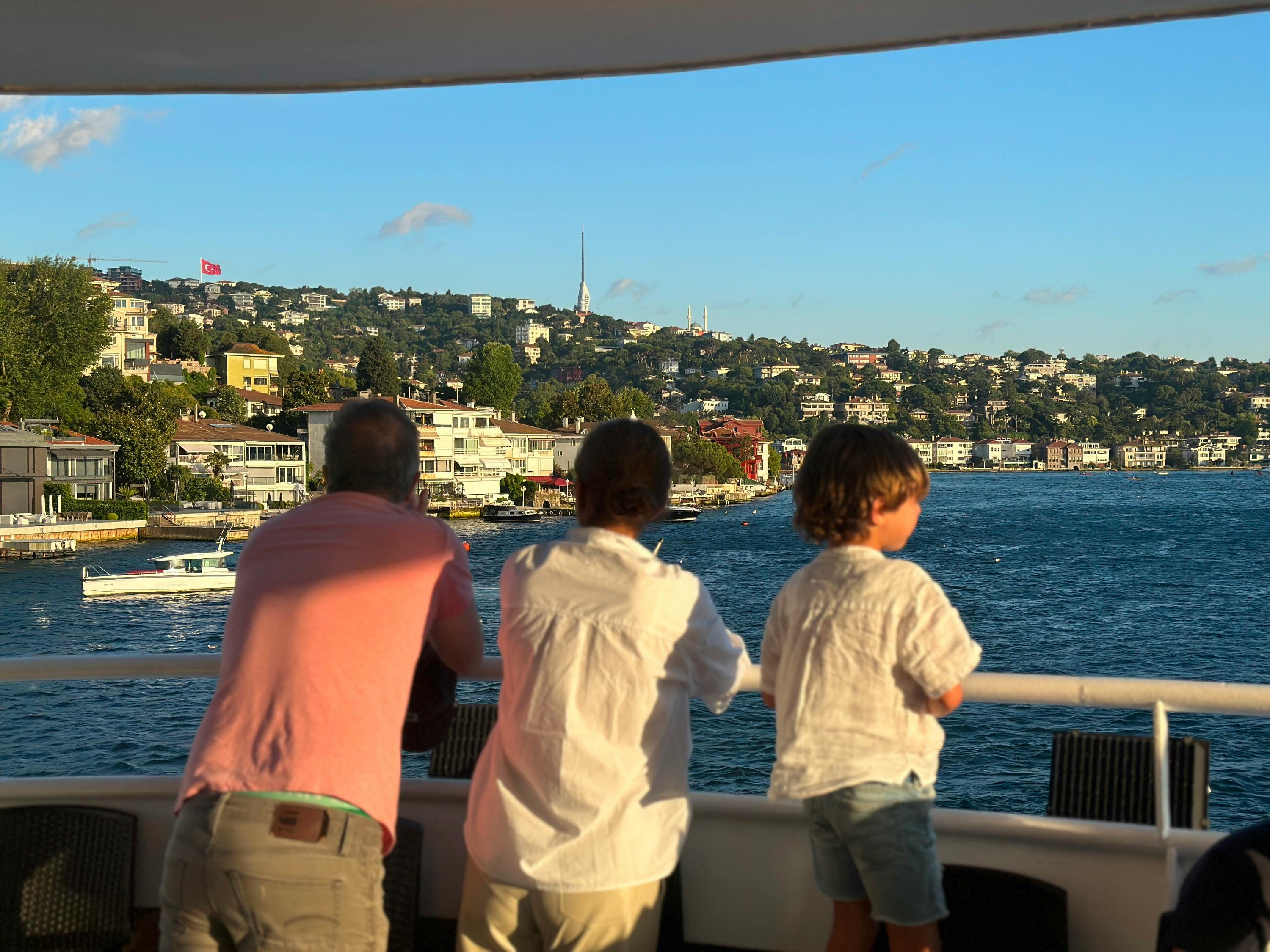 People on a boat looking at a coastal town across a body of water under a clear sky.