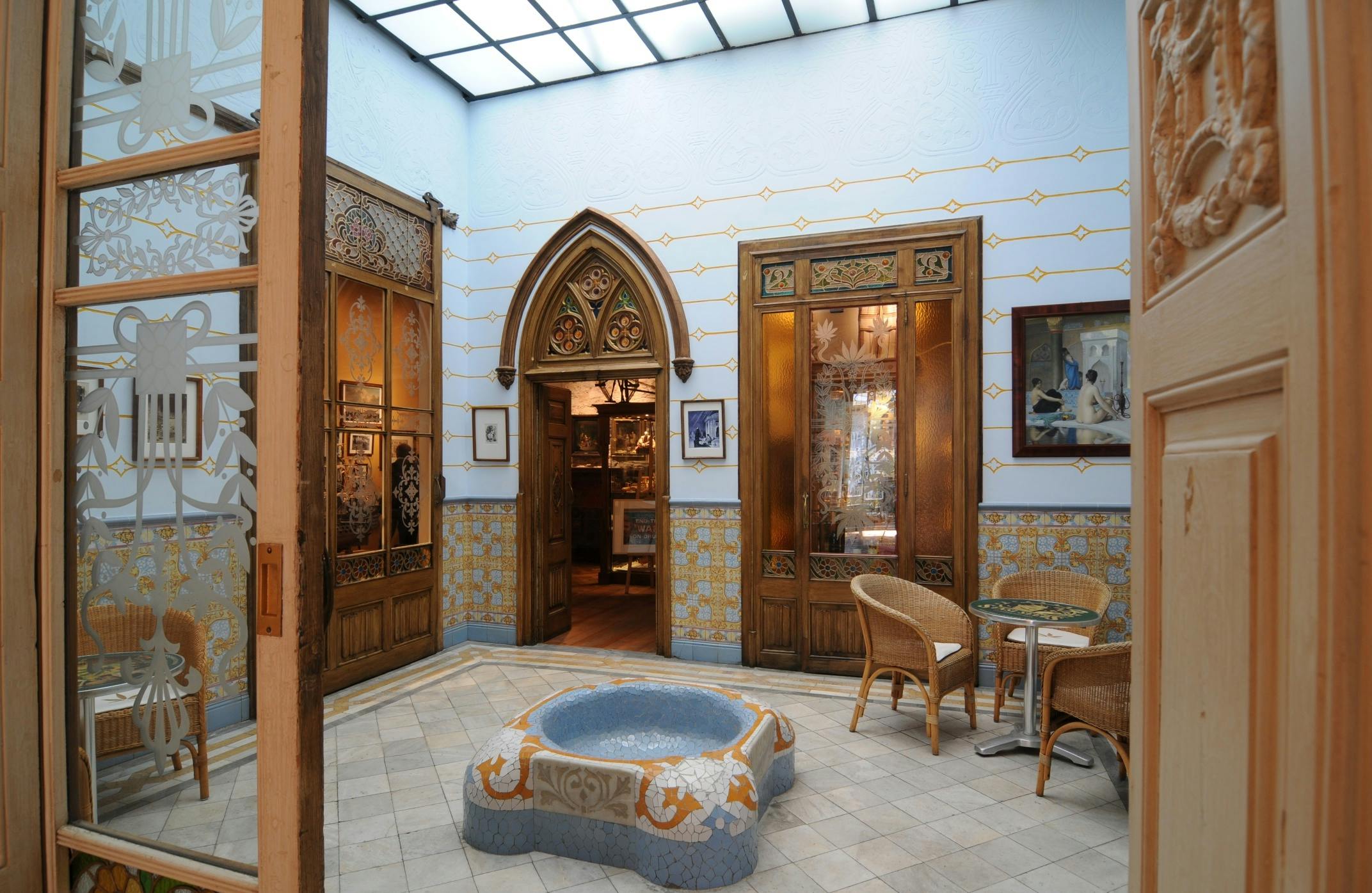 Un atrium décoratif avec des murs et des sols carrelés, une fontaine en mosaïque, des chaises en osier et des portes en bois vitrées.