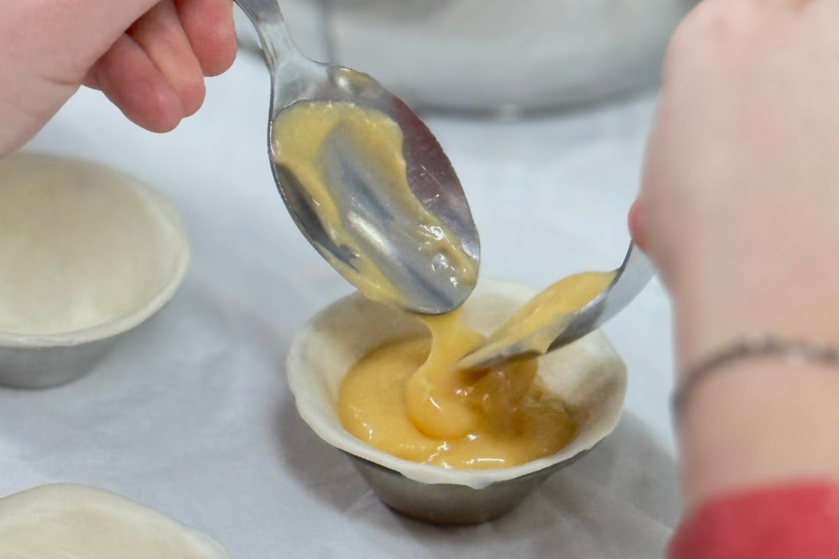 Крупным планом с помощью двух ложек наполните небольшую кондитерскую оболочку толстым желтым тестом.