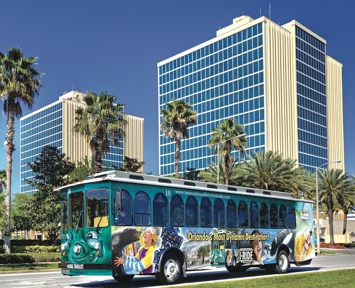 Na ulici před vysokými budovami a palmami ve slunném prostředí je vyzdobený vozík se zeleným průčelím.