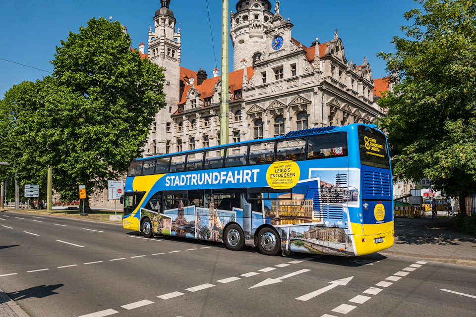 A blue and yellow double-decker bus with "STADTRUNDFAHRT" and city images is near a historic building in a city street.