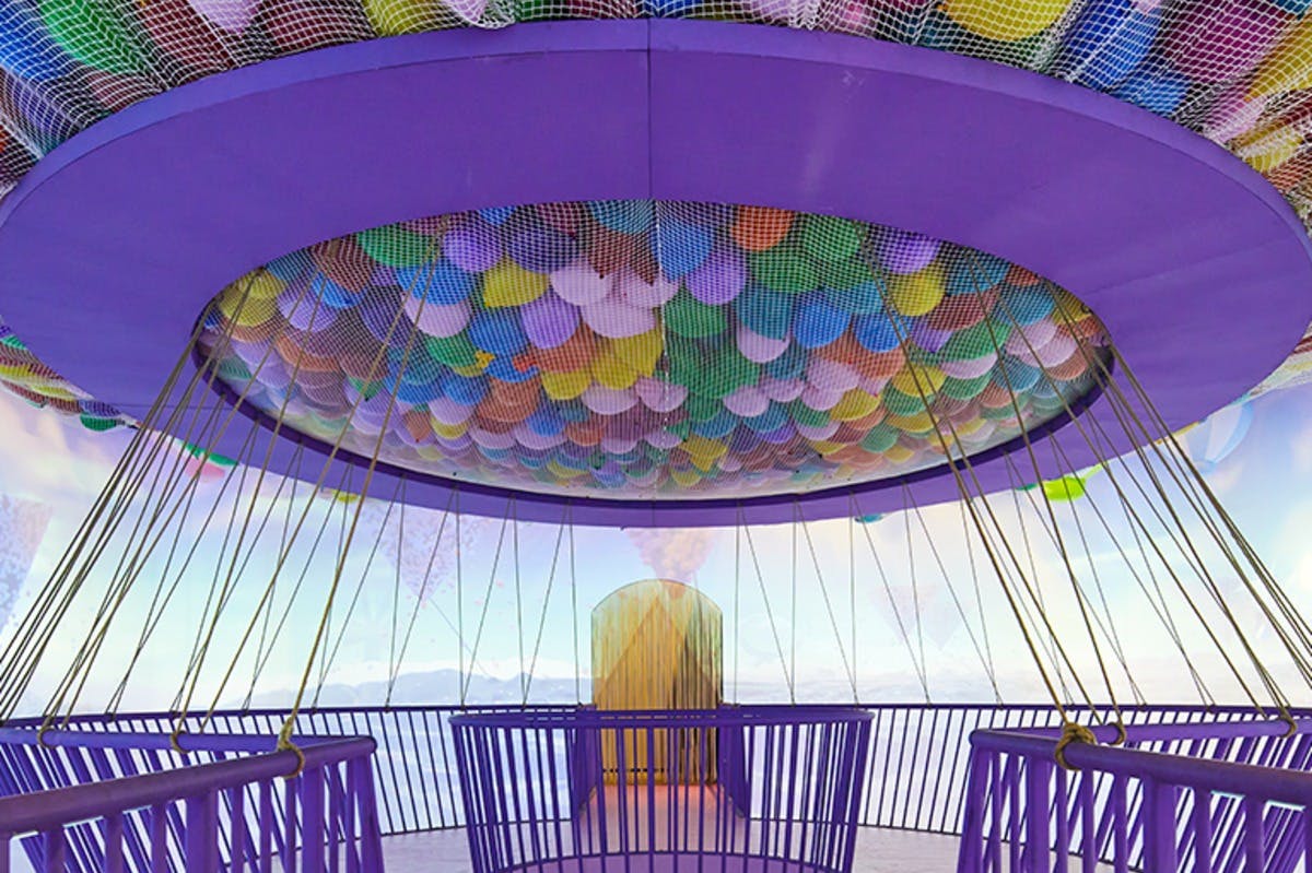 一个带栏杆、绳索和天花板的紫色圆形平台，天花板上围着网状彩色气球。