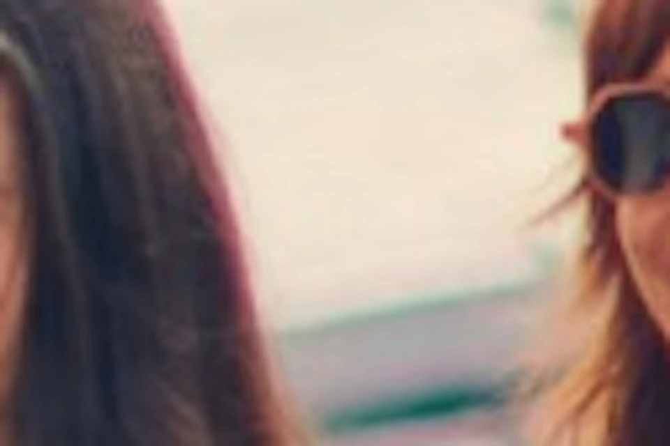 Three women pose for a selfie on a rooftop with a cityscape and greenery in the background; another woman stands nearby.