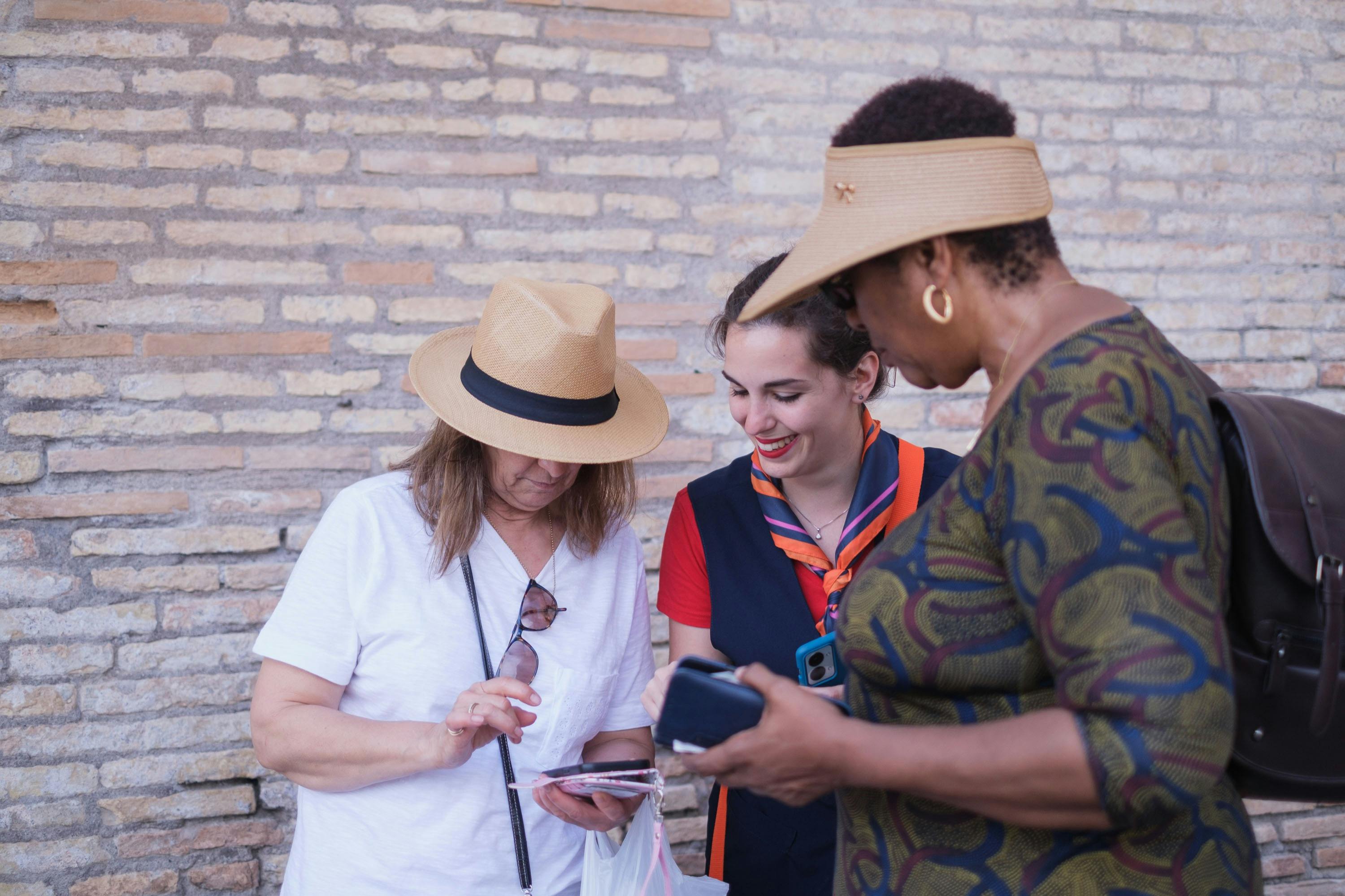 Três mulheres estão juntas, uma com um uniforme azul, sorrindo, e duas outras a olhar para algo que têm nas mãos.