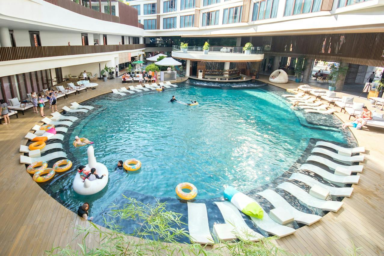 Circular pool surrounded by lounge chairs and a bar area, with people swimming and relaxing in the water.