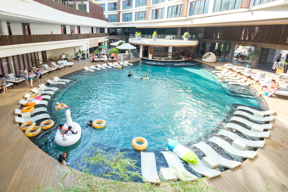 Circular pool surrounded by lounge chairs and a bar area, with people swimming and relaxing in the water.