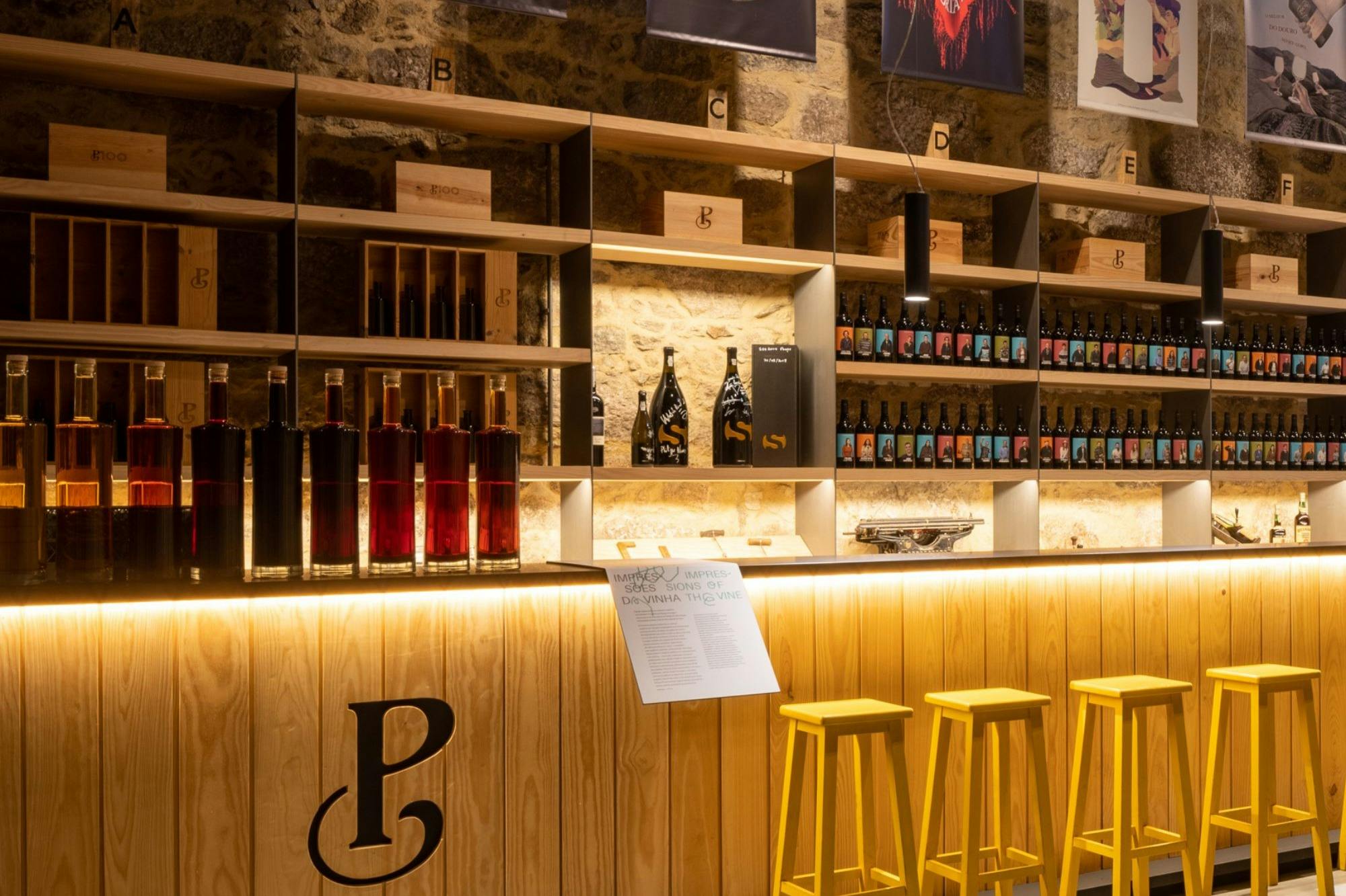 A modern bar with wooden shelves displaying bottles, illuminated counters, and yellow bar stools in a cosy setting.