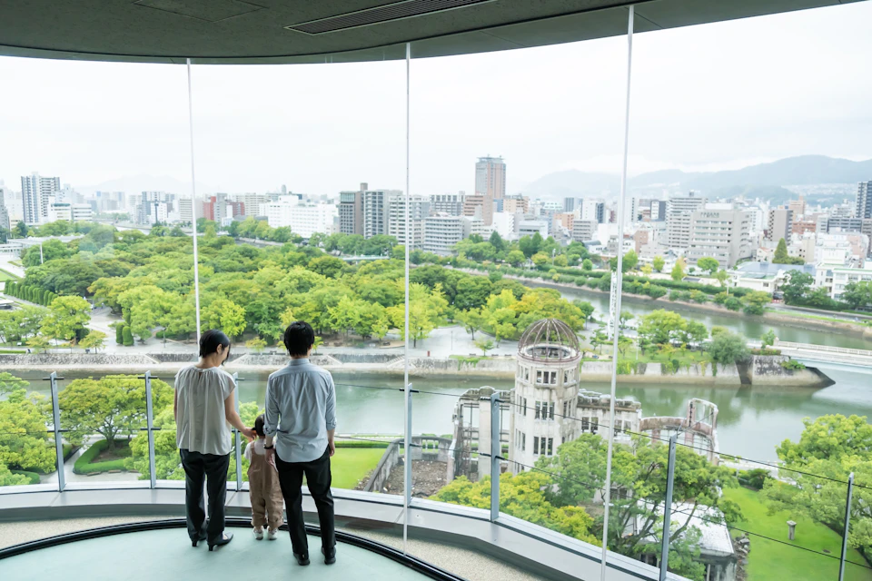 A family standing in front of a large window, overlooking a cityscape with trees, a river, and a historic dome structure.