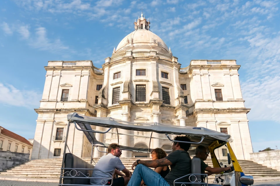 A group of people sitting in a covered cart in front of a historic domed building under a blue sky.