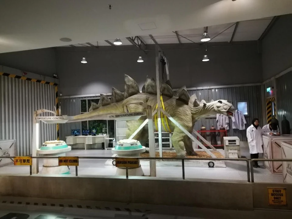 A life-sized stegosaurus replica in a laboratory exhibit with scientific equipment and warning signs around it.