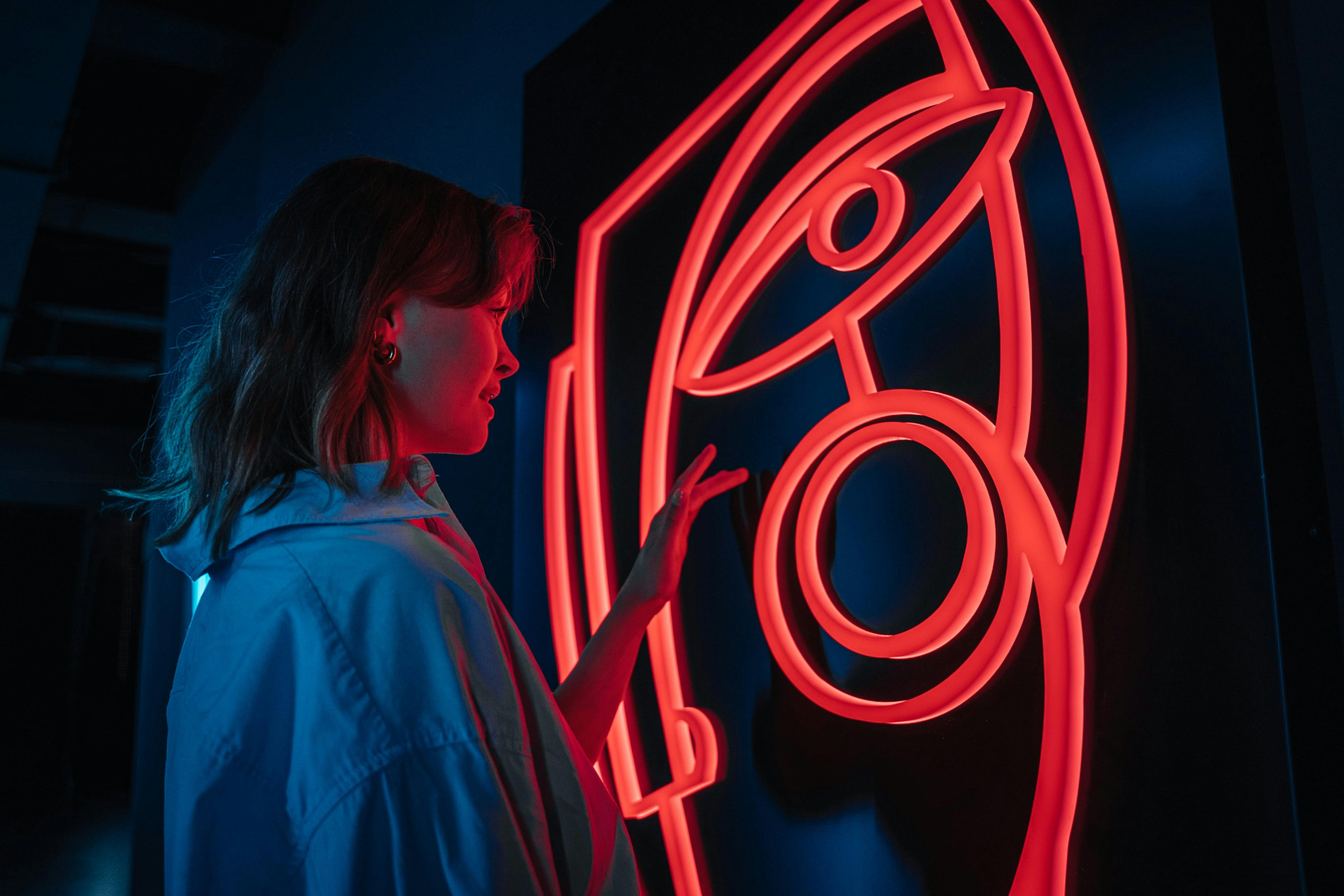 Osoba w niebieskiej koszuli dotyka świecącą, czerwoną, abstrakcyjną grafikę z motywem oczu i kółek na ciemnym tle.