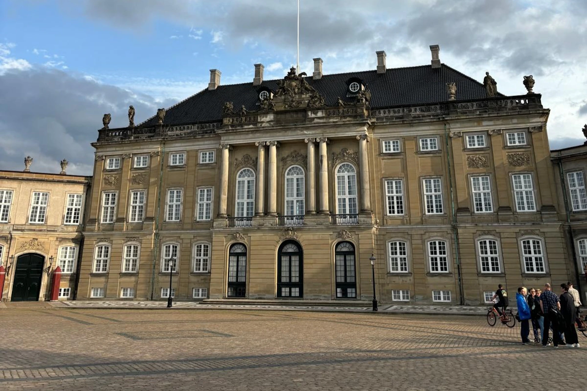 A large, ornate building with columns and statues, featuring many windows and a tiled roof, seen on a clear day with some clouds.